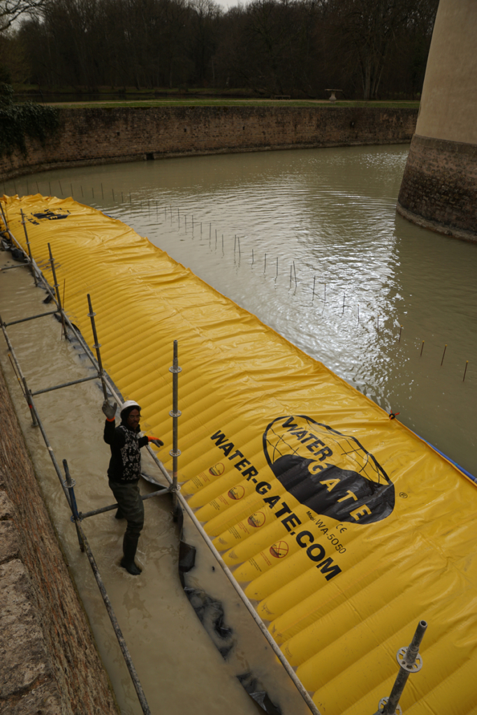 Batardeau souple partiellement rempli montrant la ligne d’eau et la toile en pression dans les douves du château